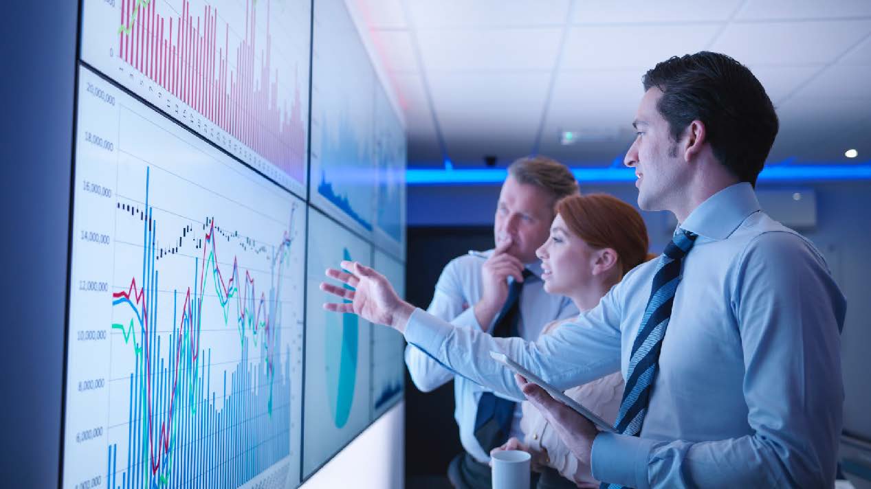 Three professionals looking at a stock chart on a large screen 